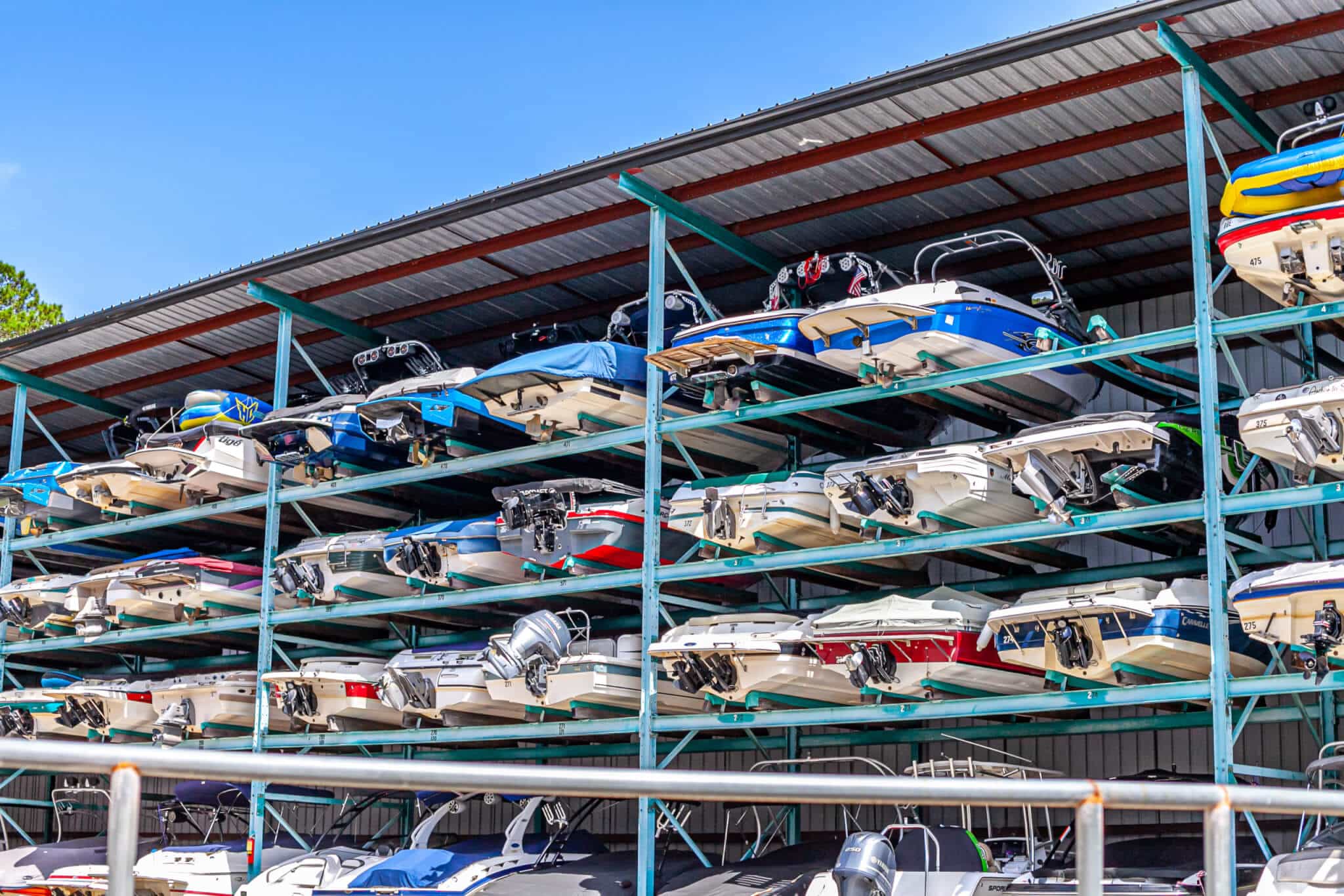 IMG_5842-scaled Stacked motorboats stored in a marina rack under a metal roof on a sunny day. | Sky Rye Design Stacked motorboats stored in a marina rack under a metal roof on a sunny day.