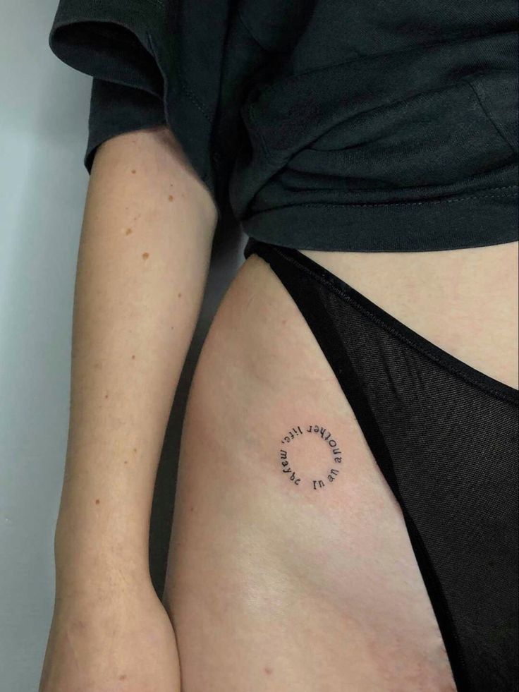 Minimalist hip tattoo with text in circular design on person's side near black underwear.