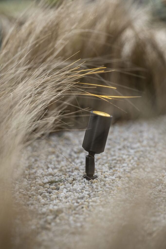 Outdoor spotlight illuminating decorative landscape with pebbles and tall grass.