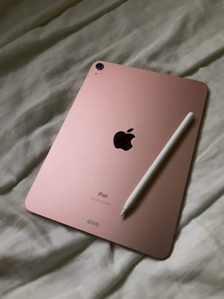 Rose gold iPad with Apple Pencil resting on a bed, showcasing modern tablet design and technology.