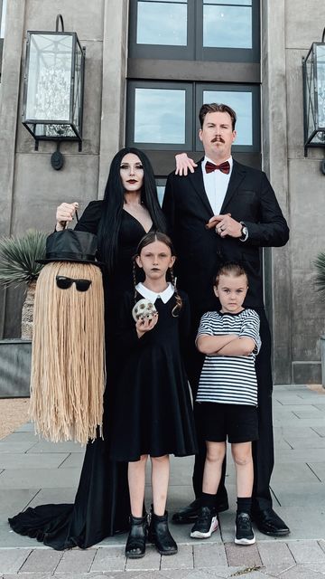 Family in spooky costumes posing for Halloween in front of a house.