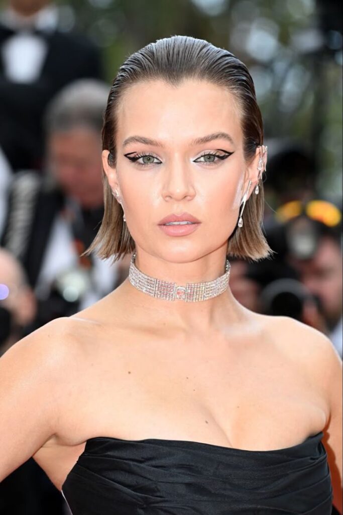 Elegant woman in a black dress with slicked-back hair and bold eyeliner at a glamorous event.