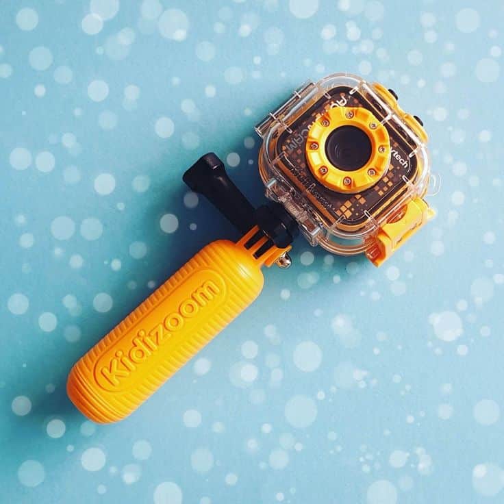 Yellow Kidizoom action camera with handle against a blue background with white spots.