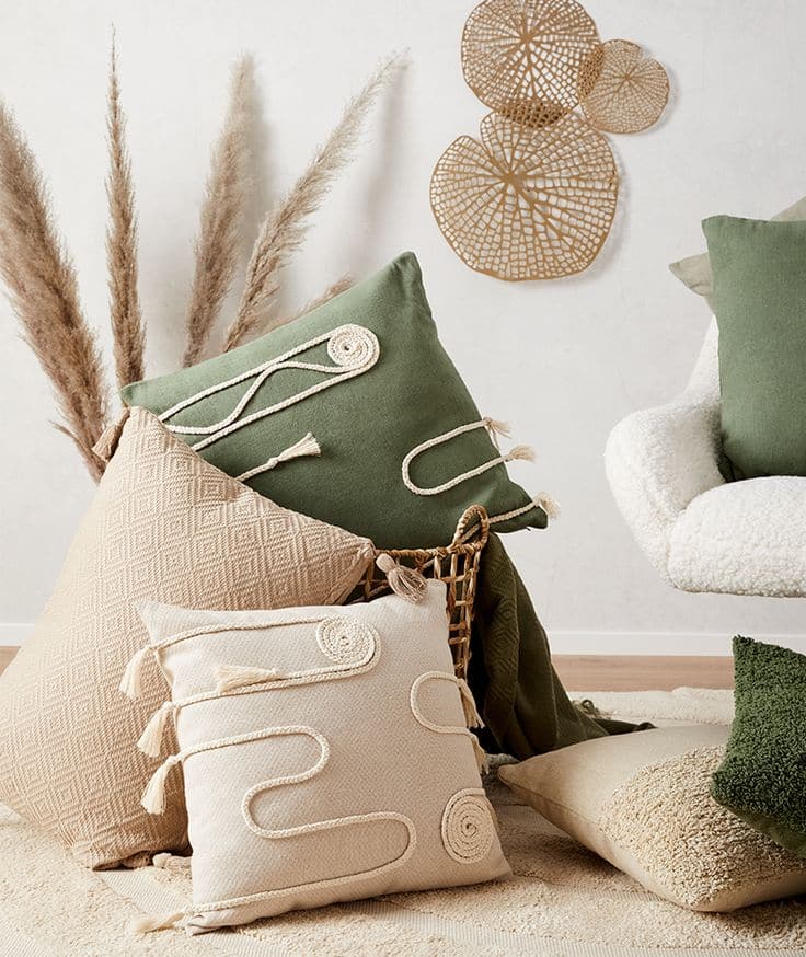 Cozy living room decor with textured throw pillows, wicker wall art, and pampas grass accents in a neutral setting.