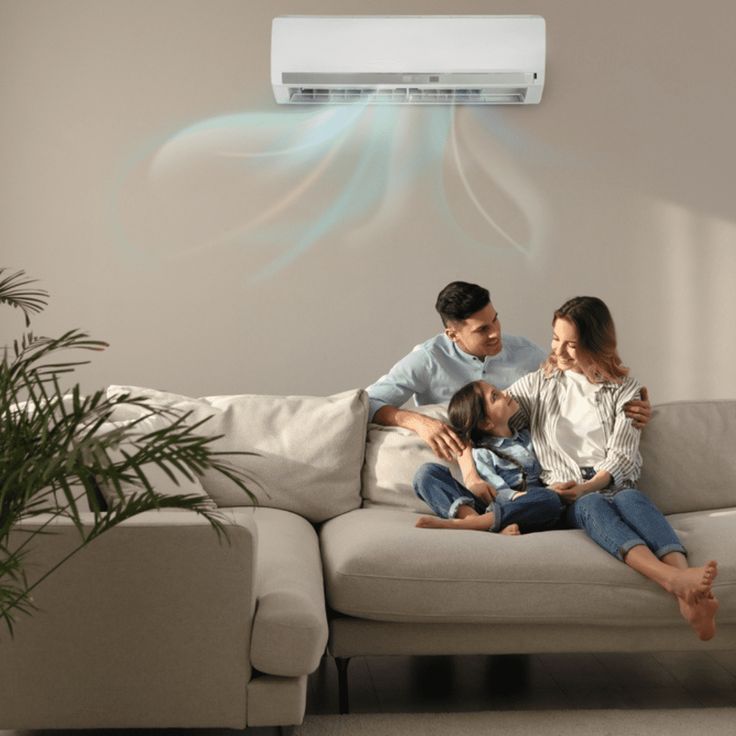 Family relaxing on a sofa under an air conditioner, enjoying cool air in a cozy living room setting.