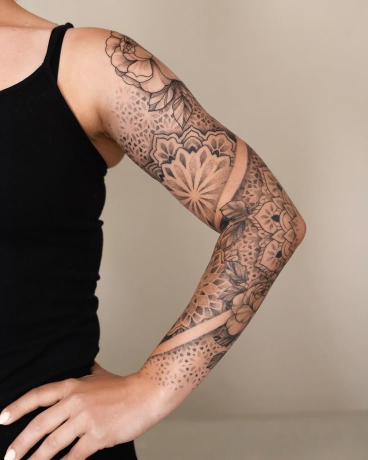 Sleeve tattoo featuring intricate floral and geometric patterns on a person's arm, wearing a black tank top.