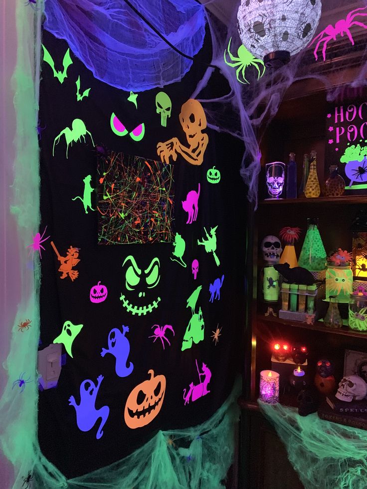 Glowing Halloween decorations with neon ghosts, skeletons, and pumpkins on a black backdrop, surrounded by cobwebs.