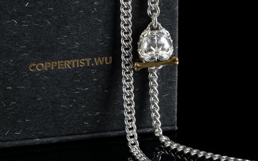 Silver skull necklace with bone, by COPPERTIST.WU on black textured background.