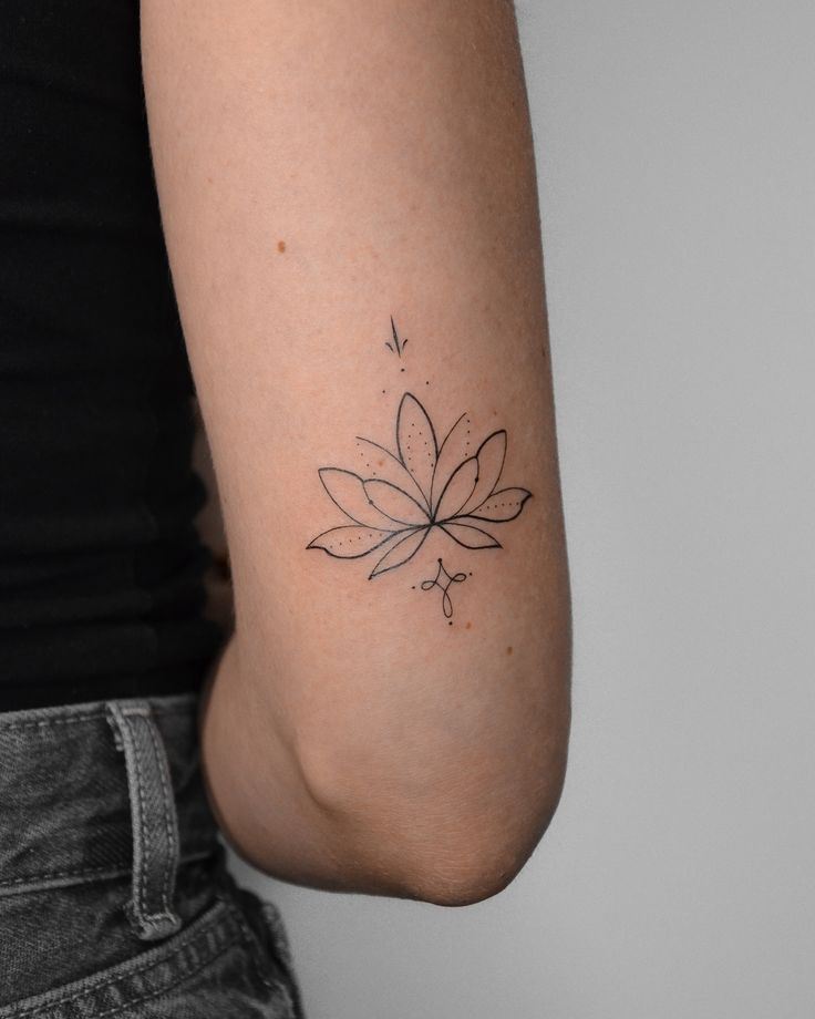 Minimalist lotus tattoo on the back of an arm, showcasing delicate line art and dots on a gray background.