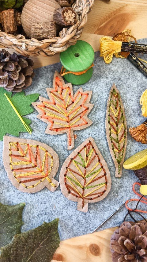 DIY embroidered felt leaves with autumn colors, surrounded by craft materials on a wooden table.