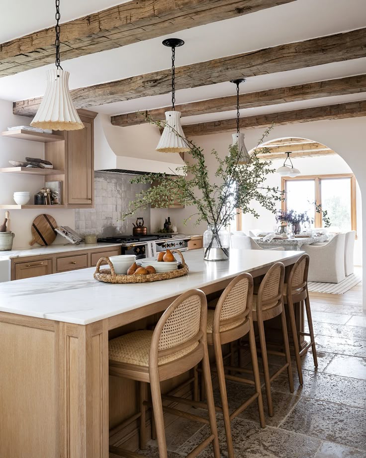 Modern farmhouse kitchen with wooden beams, island seating, rustic decor, and ample natural light from large windows.