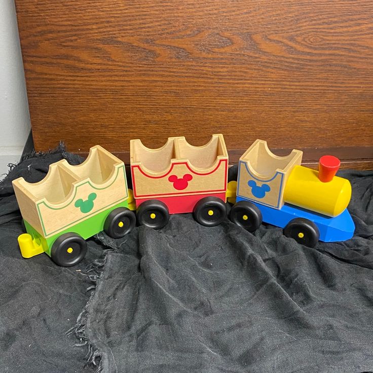 Colorful wooden toy train with Mickey Mouse logos, featuring green, red, and blue cars on a dark fabric background.