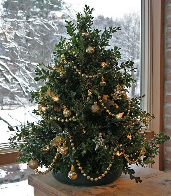 Festive green holiday tree adorned with gold ornaments and beads, set by a snowy window.