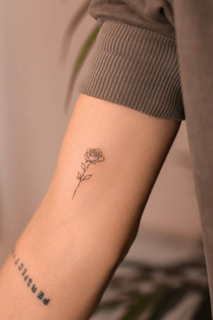 Minimalist rose tattoo on forearm, showcasing delicate black ink design with Persist text visible nearby.