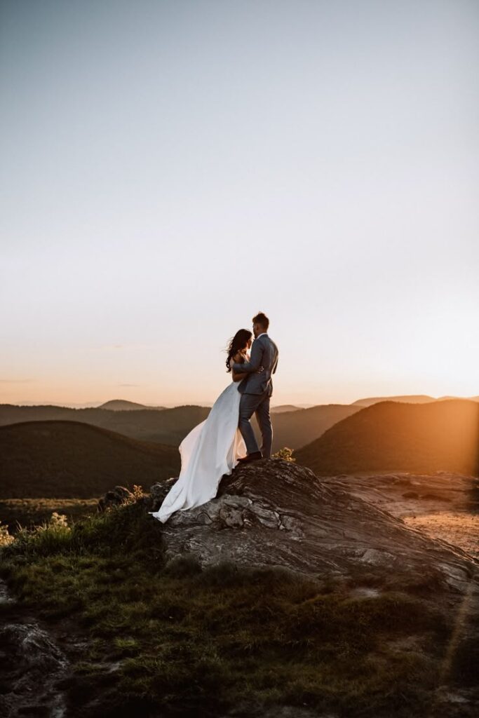 Bride and groom embrace on a mountain at sunset, wedding photo with stunning natural backdrop.