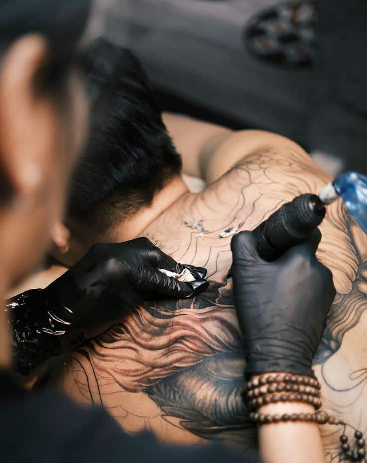 Tattoo artist in gloves creating detailed back tattoo on client, close-up.