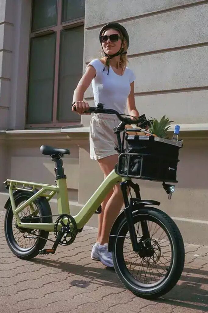 Woman with a helmet walking a green e-bike on a sunny street.