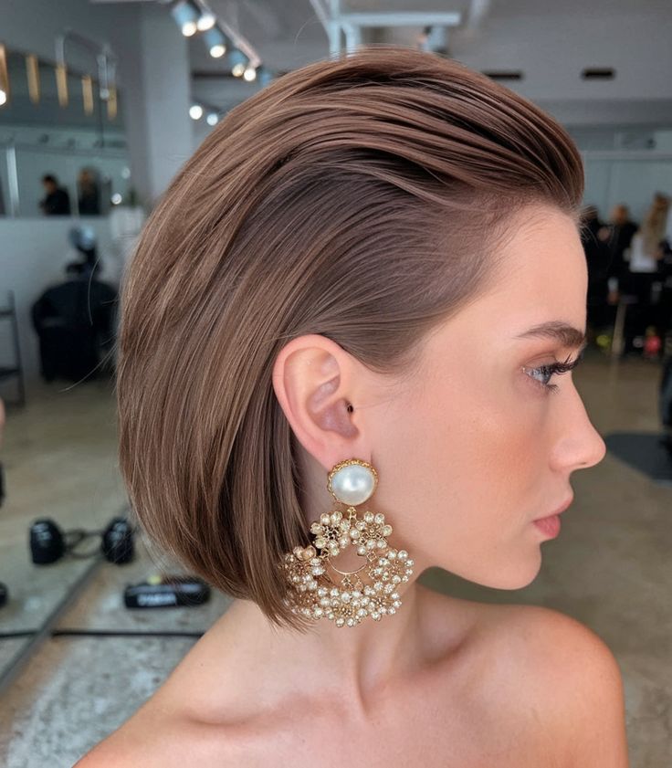 Woman with sleek bob hairstyle and statement pearl earrings in a modern salon setting.