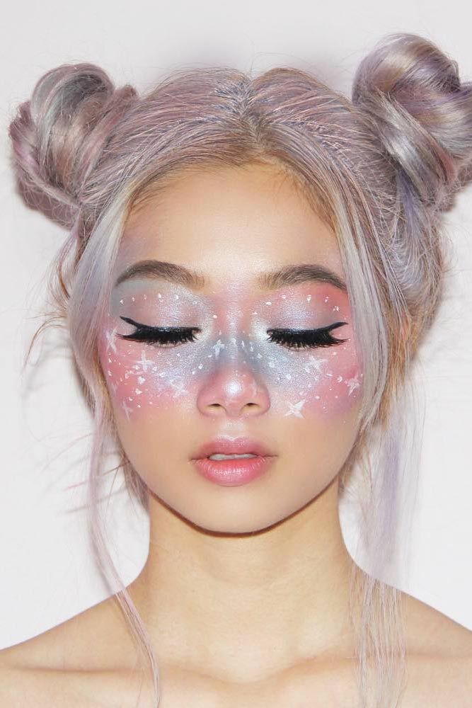 Woman with pastel galaxy makeup, space buns, and closed eyes, displaying artistic beauty style.