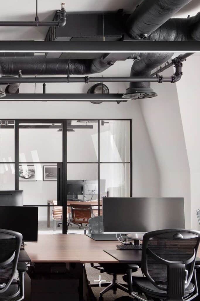 Modern office with open workstations, glass partitions, and industrial ceiling design.