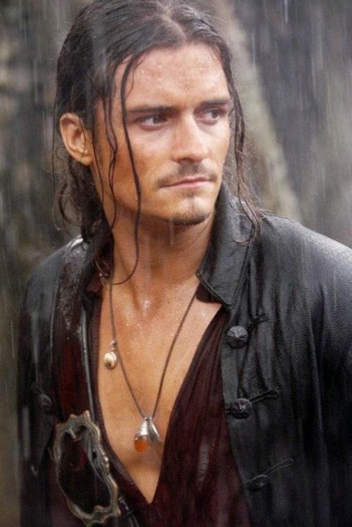 Man with wet hair and rugged attire standing in the rain, wearing a necklace, looking determinedly to the side.