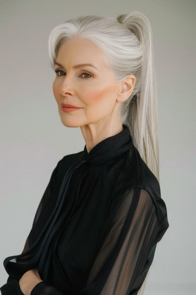 Over 60_ Try These Long Hairstyles Elegant woman with long gray hair tied in a ponytail, wearing a black blouse, looking confident. | Sky Rye Design Elegant woman with long gray hair tied in a ponytail, wearing a black blouse, looking confident.