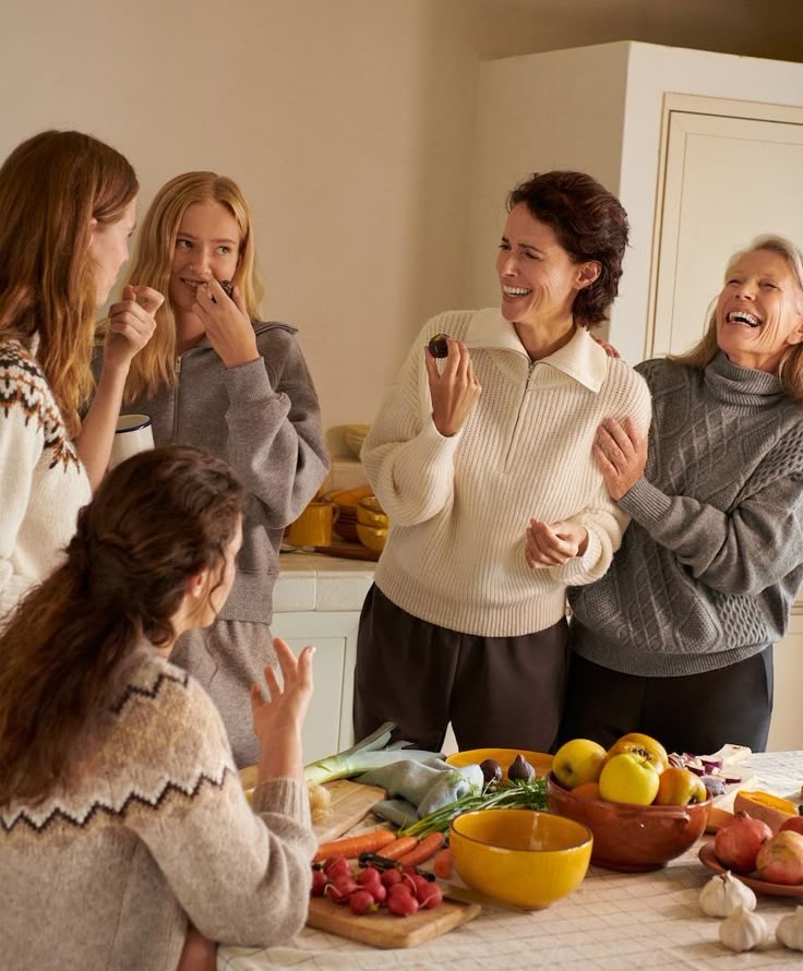 A cheerful group of women sharing a laugh in a kitchen with fresh fruits and vegetables on the table.