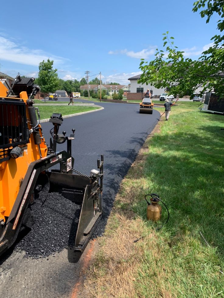 Paving machine lays new asphalt on a sunny neighborhood street, enhancing road surface quality.