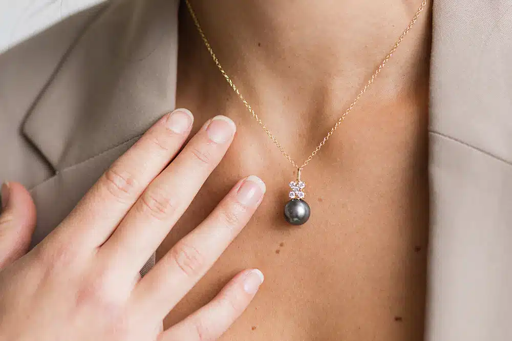 Pearl_Pendant_Trends_2025_Call_Out_e175ba5d-d9c4-4a11-b194-0e380ee50683_1200xprogressive Woman wearing a black pearl necklace pendant with diamond accents on a gold chain. | Sky Rye Design Woman wearing a black pearl necklace pendant with diamond accents on a gold chain.