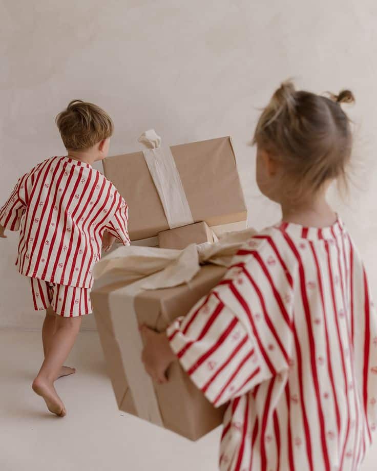 Kids in striped pajamas carrying wrapped gifts indoors.