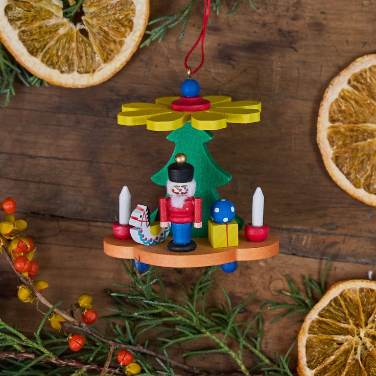 Pyramid Nutcracker German Wooden Ornament Festive nutcracker ornament with holiday decor, candles, and gifts, surrounded by dried orange slices and greenery. | Sky Rye Design Festive nutcracker ornament with holiday decor, candles, and gifts, surrounded by dried orange slices and greenery.