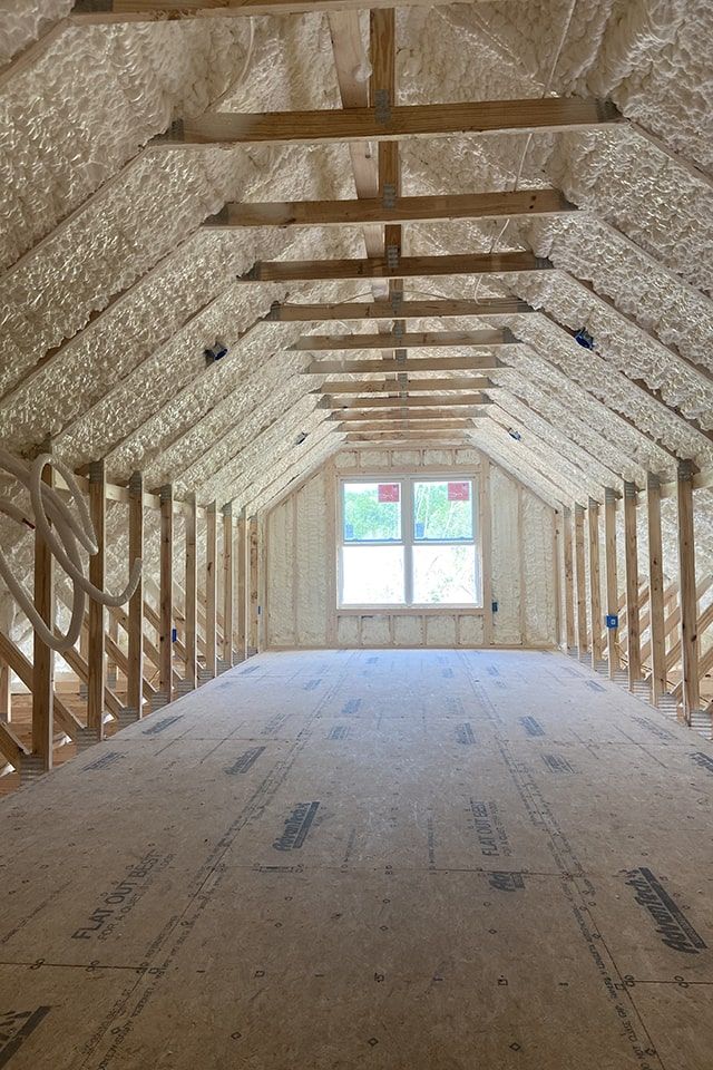 Attic with exposed foam insulation and wooden beams, ready for renovation and window installation.