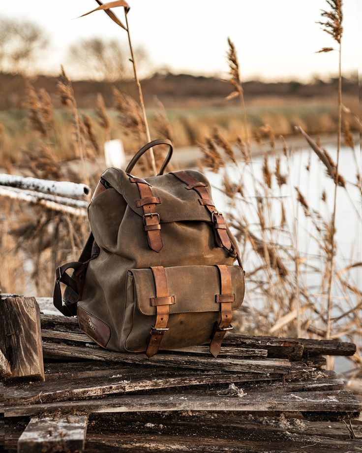 Vintage canvas backpack with leather straps on wooden planks in a rustic outdoor setting.