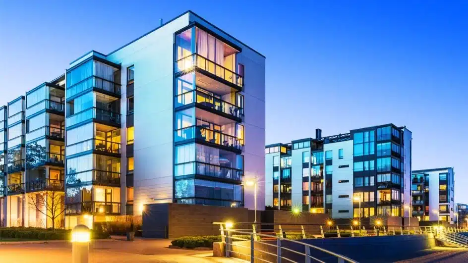Real+Esta Modern apartment buildings at dusk with illuminated windows against a clear blue sky. | Sky Rye Design Modern apartment buildings at dusk with illuminated windows against a clear blue sky.