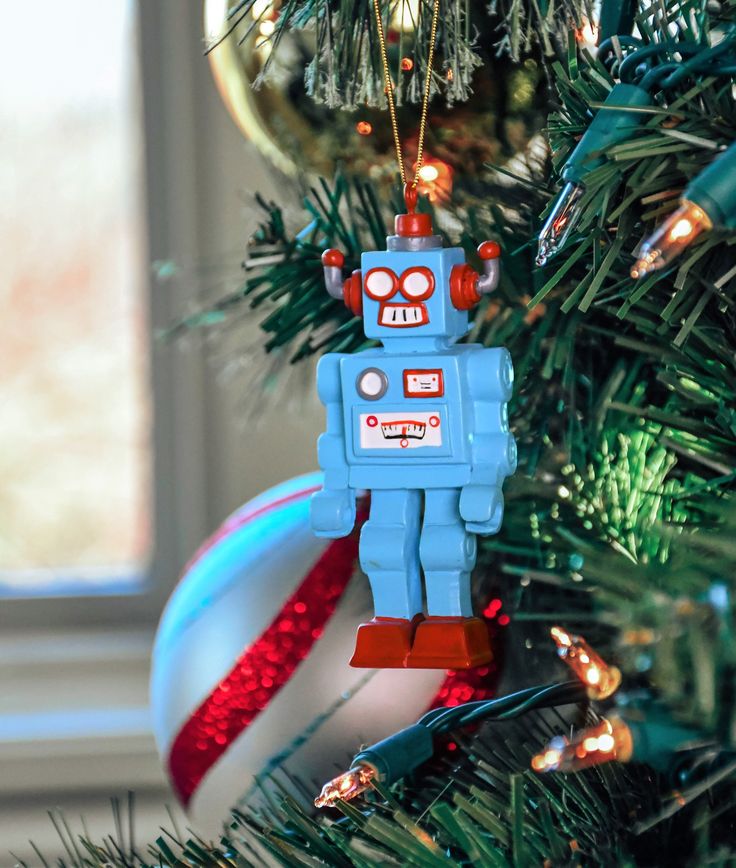 Vintage robot ornament on a decorated Christmas tree next to a striped bauble and festive lights.