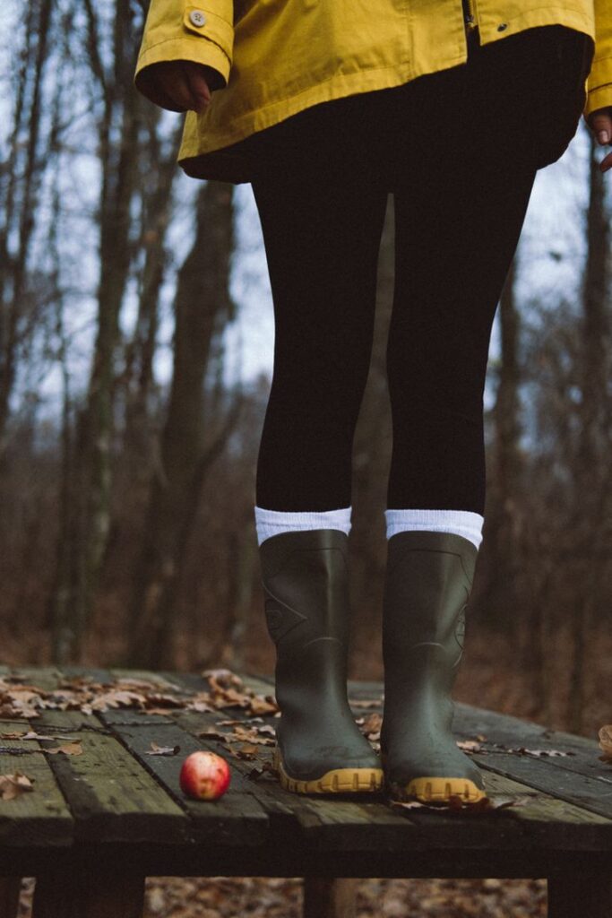 Person in yellow coat and rain boots stands on a wooden platform in a forest with red apple nearby.