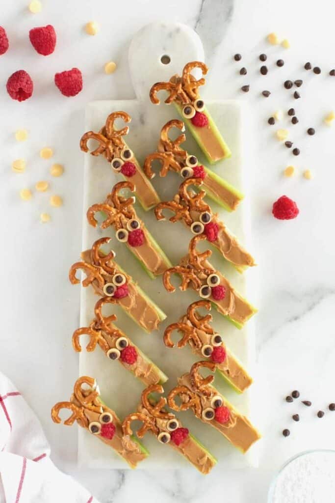Reindeer-themed snacks with pretzels, peanut butter, and raspberries on celery sticks, arranged on a serving board.