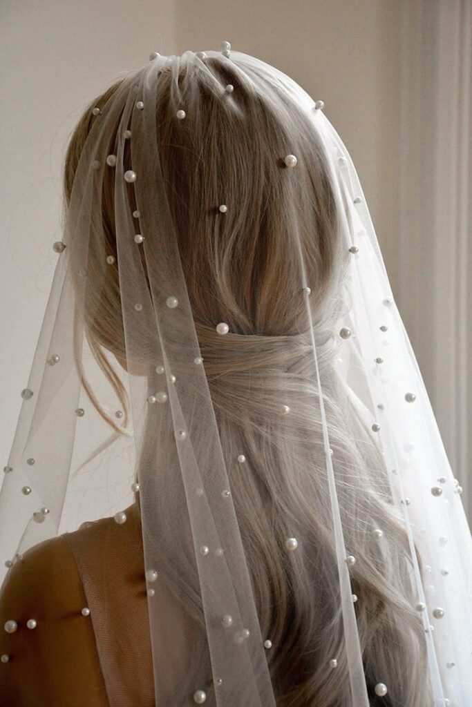 Bride with long blond hair wearing a pearl-dotted veil, showcasing elegant wedding hairstyle from the back.