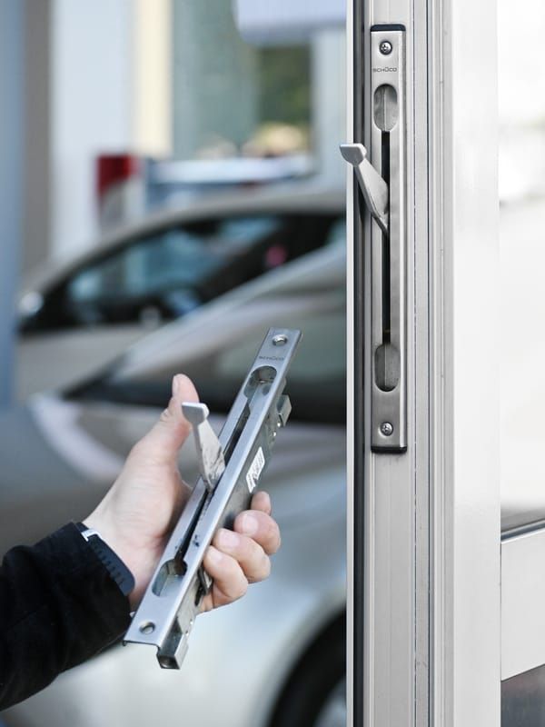 Person holding a metal door latch near a modern door for installation or repair.