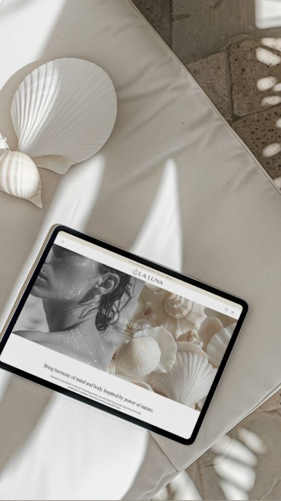 Tablet displaying La Luna website on a beige fabric with seashells, highlighting wellness theme under natural light.