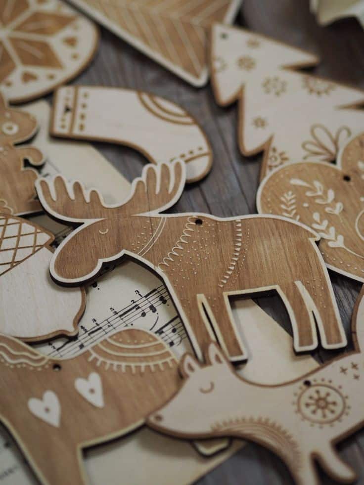 Set of 20 Wooden Christmas Ornaments Natural Holiday Decorations Rustic Folk Christmas Tree Ornaments Scandinavian Inspired Decorations Wooden Christmas ornaments in various shapes, including moose and trees, on a rustic background with sheet music. | Sky Rye Design Wooden Christmas ornaments in various shapes, including moose and trees, on a rustic background with sheet music.