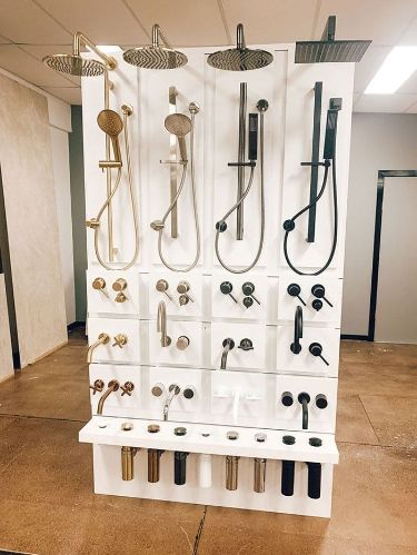 Display of various showerheads and faucets in a showroom, featuring different styles and finishes on a white stand.