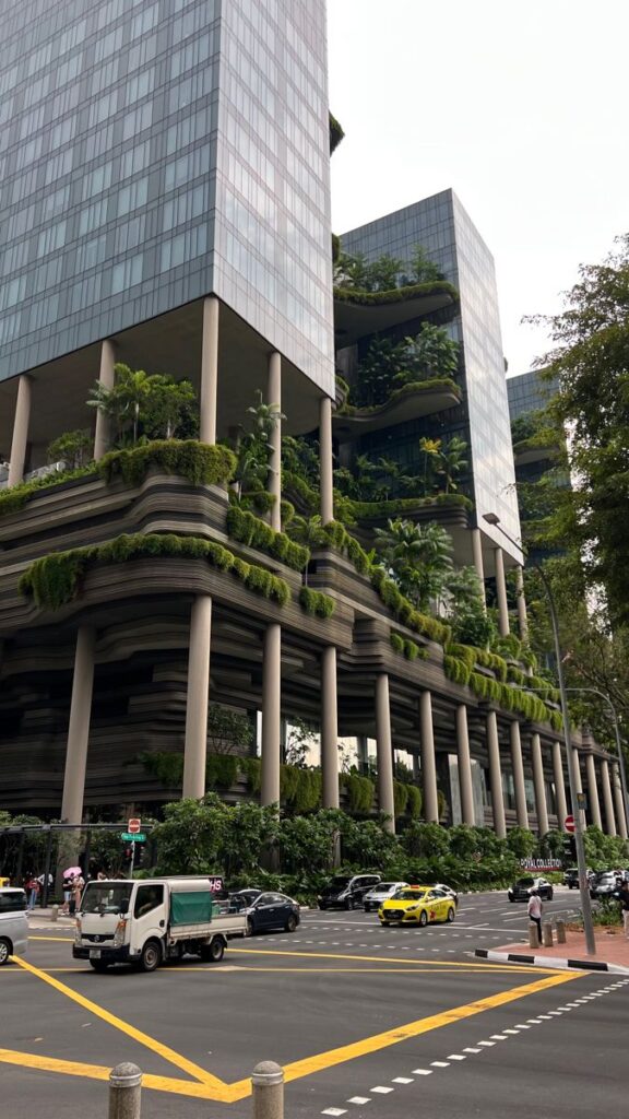 Modern urban building with lush vertical gardens and glass facade, intersected by a busy city street with vehicles. Urban design