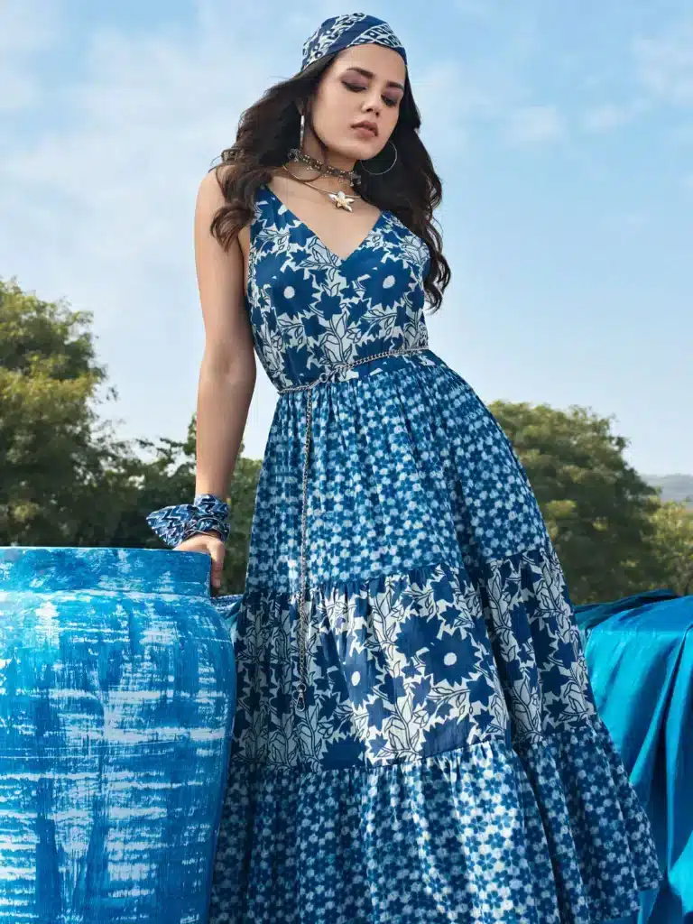 Sku29443O_7dbfdcb2-d8e2-4dac-8c4a-2101a18e07be Woman in floral blue dress and headscarf standing beside a blue pot outdoors, showcasing summer fashion. | Sky Rye Design Woman in floral blue dress and headscarf standing beside a blue pot outdoors, showcasing summer fashion.