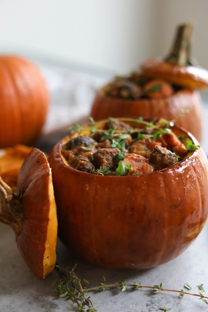Stuffed pumpkin with savory beef stew and herbs, served in a roasted pumpkin shell on a gray countertop.