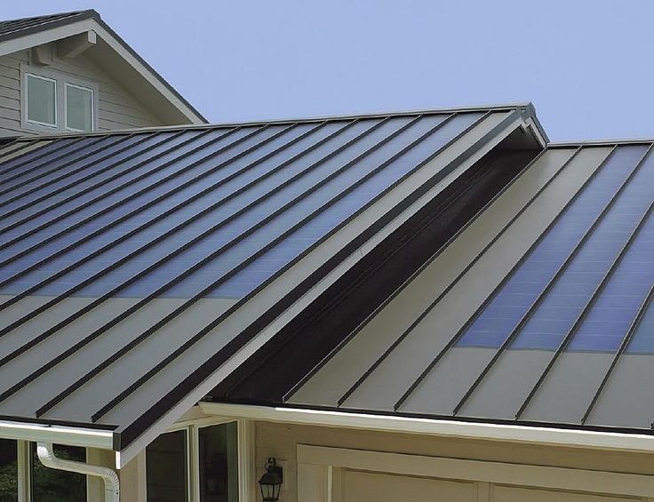 Modern house with a sleek metal roof and integrated solar panels under a clear blue sky.