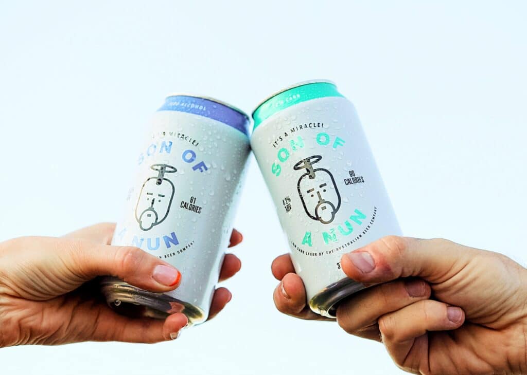 Son-of-a-Nun-for-Website6 Two hands toasting with Son of a Nun beer cans against a clear sky. | Sky Rye Design Two hands toasting with Son of a Nun beer cans against a clear sky.