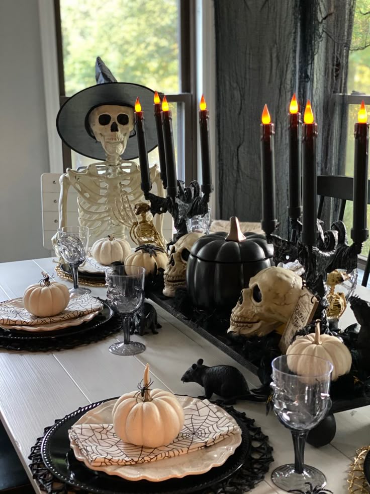 Halloween-themed table with skeleton, jack-o'-lanterns, skulls, black candles, and festive dinnerware.