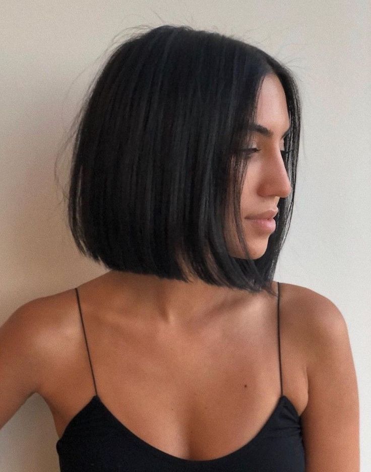 Woman with sleek black bob hairstyle, wearing a thin-strapped top, side profile against a plain background.
