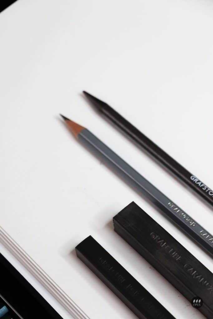 Drawing pencils and charcoal sticks on a white sheet, perfect for art and sketching projects.